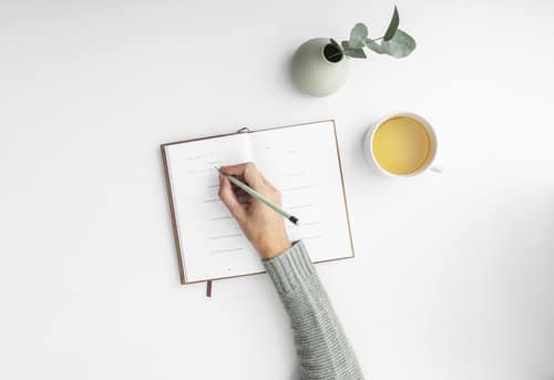 A virtual assistant writes in a diary with a herbal tea by their side